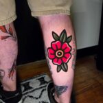Traditional red flower tattoo with green leaves on a person's lower leg
