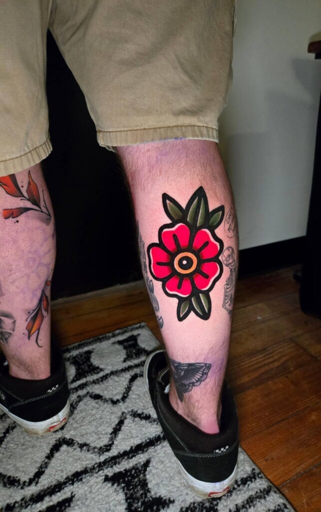 Traditional red flower tattoo with green leaves on a person's lower leg