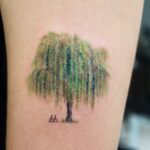 Willow tree tattoo with green leaves and small mountains on a person's arm
