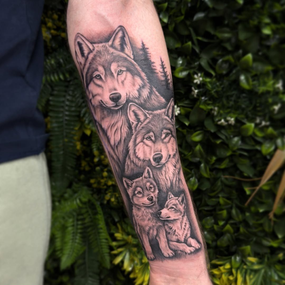 Realistic black and grey tattoo of a wolf pack on a man's forearm.